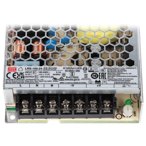 Zasilacz impulsowy z metalową obudową o strukturze plastra miodu, widoczny z góry. Na obudowie znajdują się oznaczenia techniczne i certyfikaty, a na dole widoczne są zaciski do podłączenia przewodów.