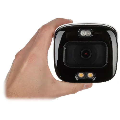 Osoba trzyma w dłoni czarną kamerę monitoringu z widocznymi diodami LED. Kamera ma błyszczącą obudowę i centralnie umieszczony obiektyw.