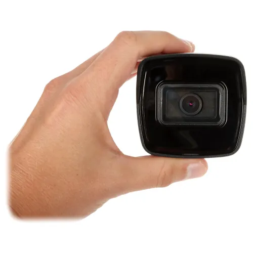 Zdjęcie przedstawia rękę trzymającą niewielką kamerę samochodową z widocznym obiektywem. Kamera ma prostokątny kształt i czarną obudowę.