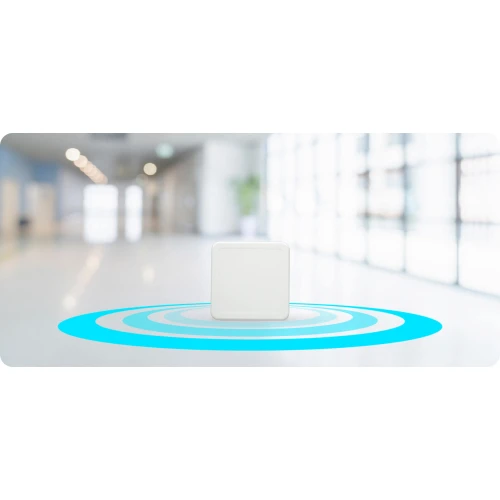 Na zdjęciu znajduje się biały, kwadratowy bezprzewodowy punkt dostępu umieszczony na tle rozmytego, nowoczesnego wnętrza budynku. Wokół urządzenia widoczny jest niebieski, koncentryczny wzór symbolizujący zasięg sygnału.