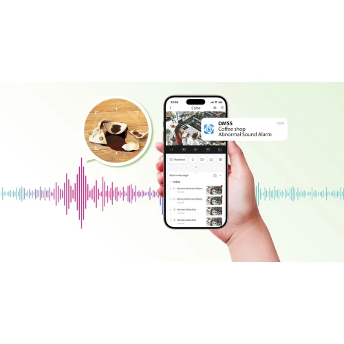 Osoba trzyma smartfon z aplikacją pokazującą alert o nietypowym dźwięku w kawiarni. W tle widoczna jest grafika z filiżankami kawy na drewnianym stole oraz kolorowe fale dźwiękowe.