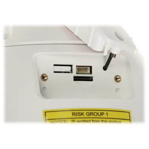 Zbliżenie na panel urządzenia z gniazdem na kartę pamięci, portem USB oraz przyciskiem reset. W dolnej części widoczna jest żółta naklejka z ostrzeżeniem "RISK GROUP 1".