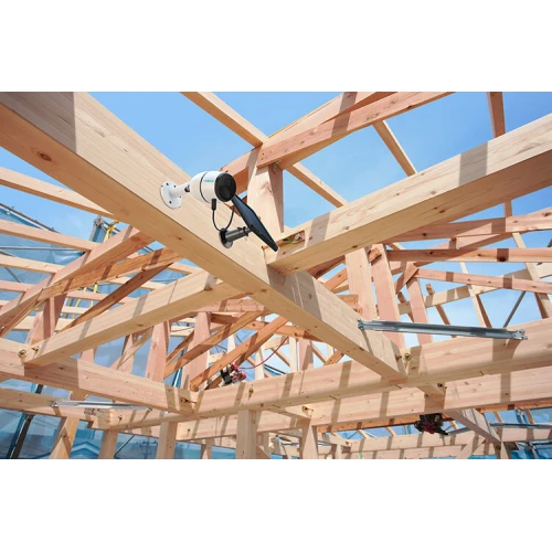 Na zdjęciu znajduje się zewnętrzna kamera IP Reolink zamontowana na drewnianej konstrukcji dachu. Kamera jest skierowana w dół, co pozwala na monitorowanie otoczenia.