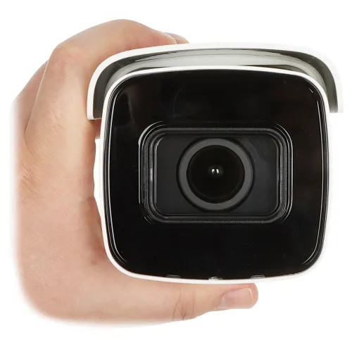 Na zdjęciu widać kamerę monitoringu trzymaną w dłoni, ukazaną z przodu. Kamera ma czarny obiektyw otoczony białą obudową.