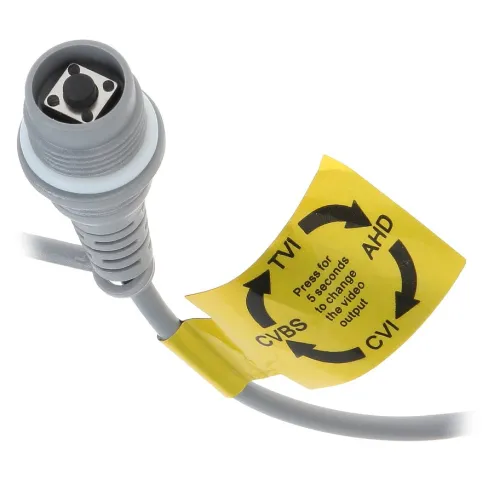 Zbliżenie na szary kabel z przyciskiem na końcu, otoczony żółtą etykietą z instrukcją zmiany standardu wideo. Etykieta pokazuje opcje: TVI, AHD, CVI, CVBS i informuje o przytrzymaniu przycisku przez 5 sekund w celu zmiany.